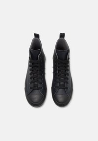 Zapatillas altas negras con parte superior de cuero suave, acentos texturizados y punta de goma; cuenta con cordones negros y un lazo en el talón.