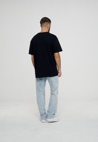 Svart bomull T-skjorte med avslappet passform, korte ermer og rund hals. Brukt sammen med lyseblå slitte jeans og hvite joggesko.
