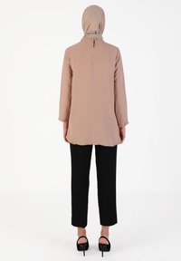 Beige lang skjorte med lange ærmer og detalje med nøglehul i ryggen, parret med sorte lige bukser og åbne sorte høje hæle.