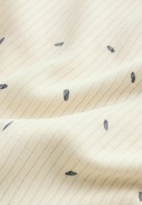 Tissu côtelé couleur crème avec de petits traits noirs dispersés et de doux plis.