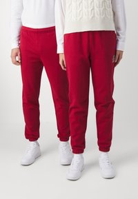 Röda bomullssweatpants med elastiska mudd och midja, prydda med en liten broderad logotyp. Kombineras med vita sneakers och en stickad tröja.