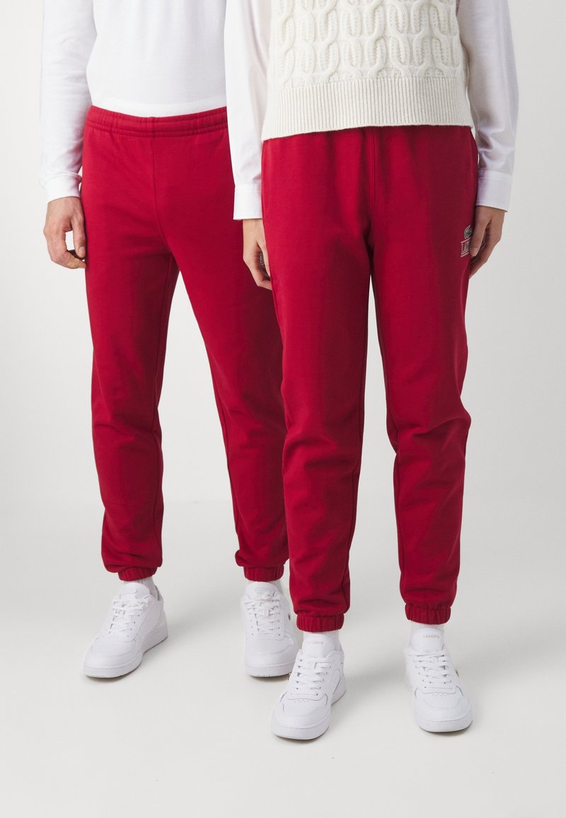 Röda bomullssweatpants med elastiska mudd och midja, prydda med en liten broderad logotyp. Kombineras med vita sneakers och en stickad tröja.