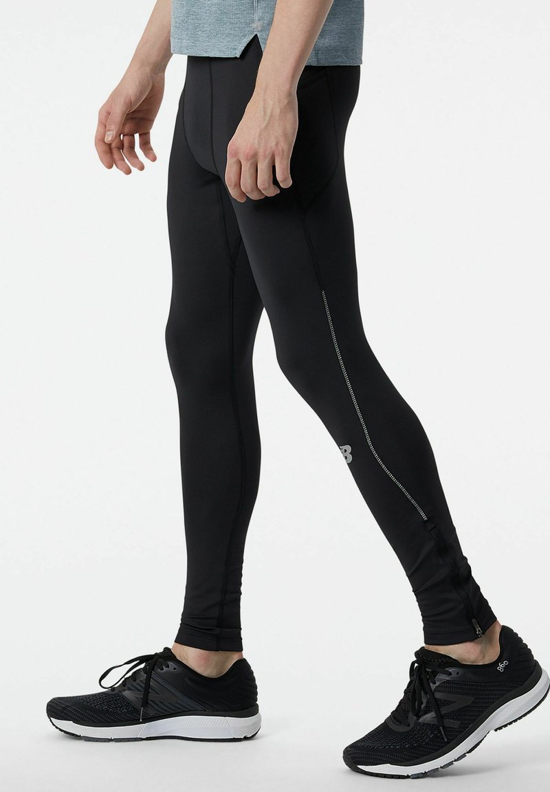 Leggings sportivi neri con un design aderente, dotati di una cerniera laterale, cuciture grigie e un logo discreto sulla parte inferiore della gamba.