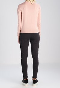 Pull en laine rose clair ajusté et pantalon slim gris foncé avec des bandes noires sur les côtés, associés à des baskets noires, vus de dos.