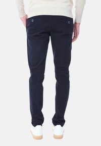 Chinos blu navy in cotone, con vestibilità slim, design con tasche posteriori dotate di bottoni, indossati con sneaker bianche.