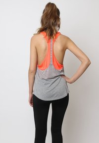 Camiseta deportiva gris sin mangas con diseño de espalda nadadora, que presenta un acento naranja brillante, hecha de tela ligera, con un dobladillo redondeado.