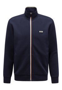 Marinblå idrottsjacka med dragkedja och hög krage, kontrasterande dragkedja och broderad "BOSS"-logotyp på vänster bröst. Mjuk tygtextur.