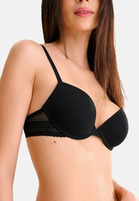 Soutien-gorge noir à armatures avec un tissu lisse, des accents en dentelle sur la bande et des bretelles ajustables. Forme cintrée pour le soutien et la couverture.