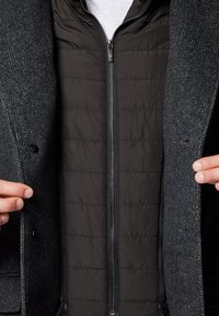 Szary teksturowany płaszcz z czarną wewnętrzną warstwą na zamek błyskawiczny. Płaszcz ma klapany kołnierz i kontrastowe materiały do izolacji.