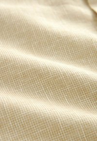 Tejido beige claro con una superficie texturizada, que presenta un sutil patrón de cuadrícula en blanco, creando una apariencia suave y suave.