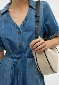 Jeanskleid mit V-Ausschnitt, kurzen Ärmeln, braunen Knöpfen und gebundenem Taillenband; kombiniert mit einer cremefarbenen Tasche mit schwarzem Rand und Lederträger.