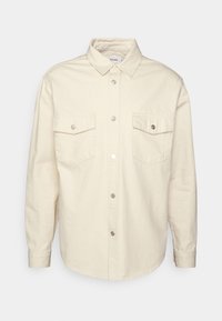 Beige button-up shirt made of cotton with a collar, two chest pockets, and snap-button closure. Soft texture with a relaxed fit.