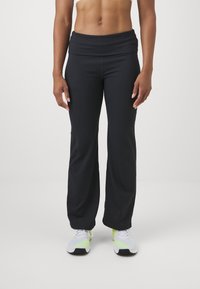 Czarne legginsy do jogi z szerokim, składanym paskiem w talii, gładką teksturą i lekko rozszerzanym krojem, w połączeniu z szarymi i neonowymi butami do biegania.