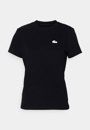 Camisa de algodão preta com mangas curtas e gola redonda, com um pequeno logo branco da Lacoste posicionado no lado esquerdo do peito.
