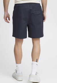 Tengerészkék elasztikus derékpántú rövidnadrág, hátsó gombos zsebbel, könnyű anyagból készült. Látható varrási részletek és laza kialakítás.