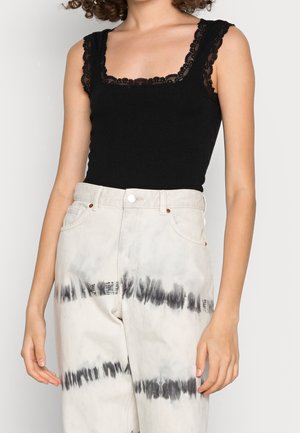 Černý žebrovaný top s krajkovým lemováním u hranatého výstřihu, kombinovaný s světle zbarvenými kalhotami s batikovaným vzorem v černých pruzích a s vysokým pasem.