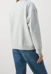 Sudadera gris con un corte holgado, escote redondeado y puños acanalados. Combinada con jeans de mezclilla azules, que presentan detalles de costura sutiles.