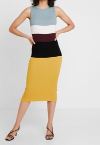 Stickad klänning med ribbad textur, som har en färgblockdesign i blått, vitt, vinrött, svart och senapsgult, med en figurnära silhuett.