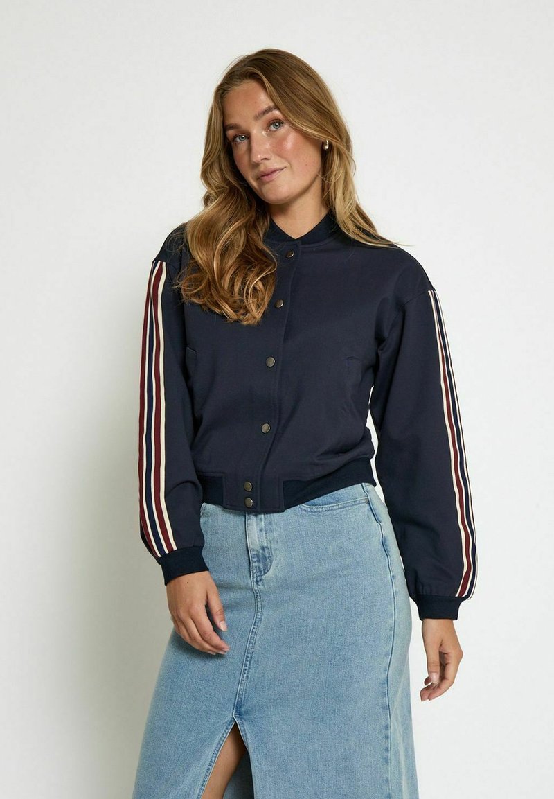 Navy bomber jacket with button closure, featuring red and white stripes on sleeves. Soft fabric, ribbed cuffs, and cropped length.