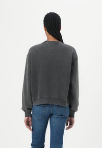 Dark gray sweatshirt with a relaxed fit, ribbed cuffs, and hem. Styled with blue jeans, showing a casual and comfortable design.