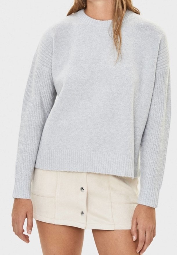 Femme portant un pull en maille côtelée gris clair à manches longues et une mini-jupe crème boutonnée devant.