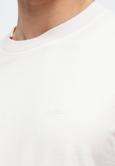 Λευκό κοντομάνικο μπλουζάκι με στρογγυλή λαιμόκοψη από απαλό βαμβάκι. Διαθέτει διακριτικό ανάγλυφο λογότυπο στο στήθος. Λεία υφή με απλό σχέδιο.