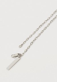 Ασημένιο κολιέ με αλυσίδα που αποτελείται από οβάλ κρίκους, με κούμπωμα και ορθογώνια ετικέτα με το χαραγμένο "FAVELA". Απαλή υφή, μινιμαλιστικό σχέδιο.