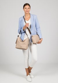 Beige suede shoulder bag and small handbag with brown straps, displayed against a plain backdrop. Features smooth textures and minimalist design.