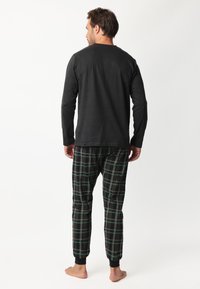 Top negro de manga larga con cuello redondo, combinado con pantalones de pijama a cuadros en verde, negro y rojo, que cuentan con tobillos ajustados para un ajuste ceñido.