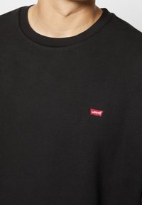 Sweat-shirt noir en coton avec un col rond, doté d'une petite étiquette rouge Levi's sur le côté inférieur gauche. Texture douce et manches longues.