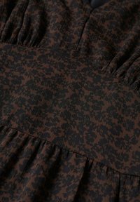 Tissu brun foncé avec petit imprimé floral noir dense et détail de couture froncée sur toute la surface.
