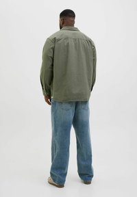 Camisa verde de manga larga con cuello, combinada con unos vaqueros de corte holgado en azul claro. El conjunto presenta puños con botones y un corte recto.