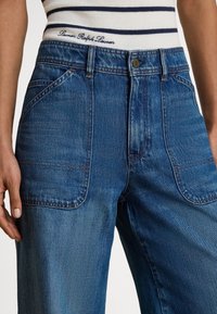 Denimbukser i mellomblå med en avslappet passform, med sidelommer og kontrastsøm. Høyt liv med logodetalj på midjen.