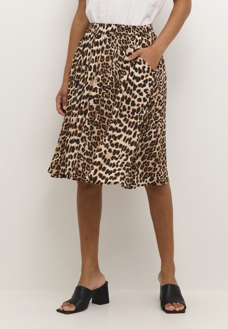 Leopard print skirt with pleats, made of lightweight fabric. Features a high waist and side pockets. Black block-heeled mules are worn.