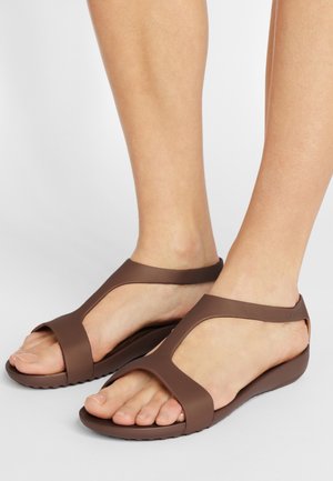 Brown rubber sandals with a T-strap design, open toe, and textured sole for grip. Features a curved silhouette and minimalistic style.