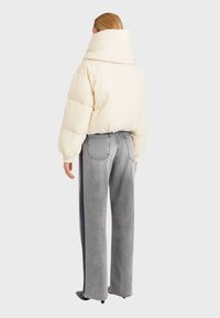 Piumino color crema con collo alto, abbinato a jeans grigi a vita alta e gamba larga, caratterizzati da una texture scolorita e tasche posteriori.