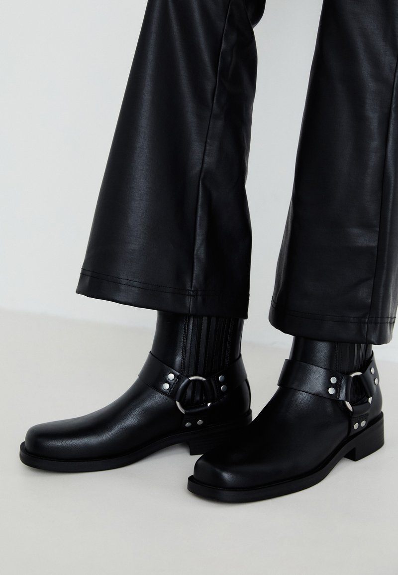 Black leather ankle boots with a rounded toe, featuring a decorative buckle and studs on the strap, and vertical ribbed detailing.