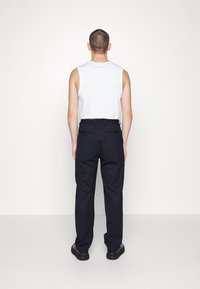 Weißes ärmelloses Shirt und dunkle marineblaue Hose mit elastischem Bund und Gesäßtaschen, von hinten betrachtet. Glattes Material und gerade geschnittene Passform.