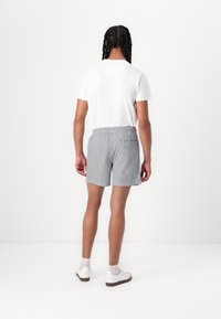 Grå og hvide stribede shorts med elastisk talje, der har en baglomme. Sammen med en simpel hvid t-shirt og hvide sneakers.