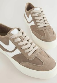 Brune ruskinds sneakers med en hvid swoosh, beige snørebånd, tekstureret mellemsål og en rund form. Har syning detaljer langs designet.