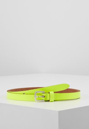 Ceinture en cuir jaune vif avec boucle rectangulaire en argent posée à plat sur une surface blanche à coins.
