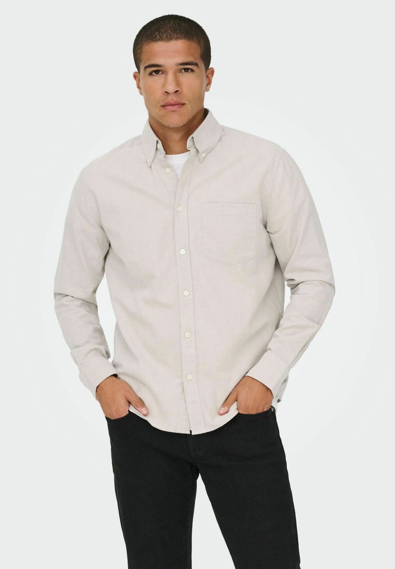 Lys grå langærmet skjorte med button-down krave, enkelt brystlomme og blød tekstur. Båret med sorte jeans.