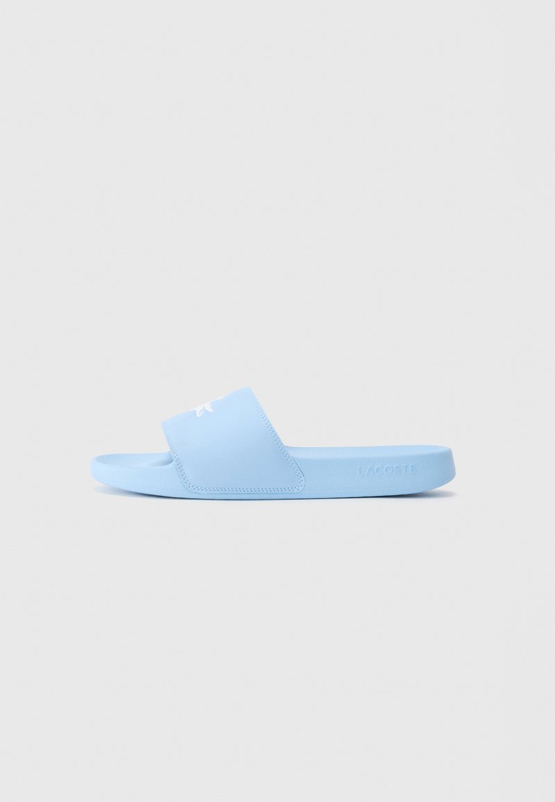 Sandalie ușor albastre, cu slip-on, dotate cu o curea lata care prezintă un logo brodat alb de crocodil și marcaj Lacoste pe marginea tălpii.