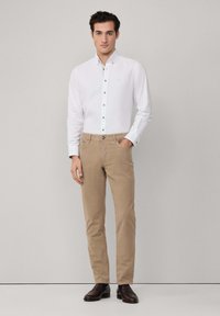 Witte button-up shirt met een kraag en bruine knopen, gedragen met khaki chinos en donkerbruine schoenen. Eenvoudig ontwerp met een fitted silhouet.