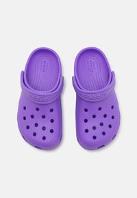 Ljubičaste gumene klompe s ventilacijskim otvorima, remenom na stražnjoj strani i teksturiranim ulošcima s "CROCS" logotipom sa strane.