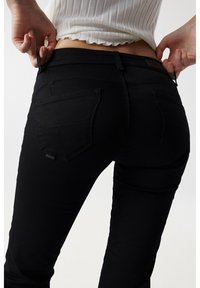 Jeans de mezclilla elástica negra con una silueta ajustada, que cuentan con dos bolsillos traseros y una pequeña etiqueta de marca en el bolsillo izquierdo.