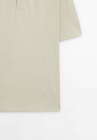 Polo beige à manches courtes avec col et patte de boutonnage, présenté sur un fond blanc.