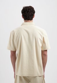 Korte mouwen blouse in lichtbeige, met een gestructureerde stof en een relaxte pasvorm, met een kraag en een boxy snit. Achteraanzicht weergegeven.