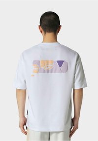 Hvit t-skjorte med kort erme som har et flerfarget abstrakt design på baksiden i lyse oransje, lilla og beige. Glatt stoftekstur.