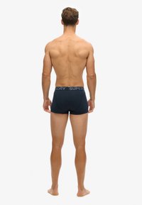 Boxer shorts bleu marine en tissu doux, avec une large taille élastique portant le logo "SUPERDRY". Modèle montré de dos.